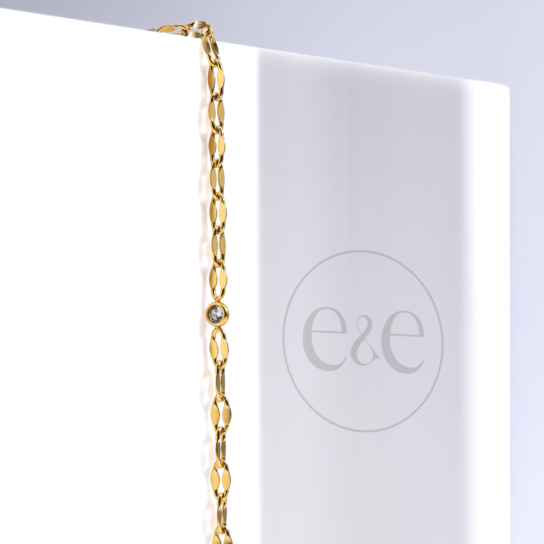 A soft, gold-tone chain with a central CZ stone is shown elegantly resting on skin, styled as both anklet and bracelet. It shimmers as the model moves gently, highlighting the chain’s flexibility and detail.