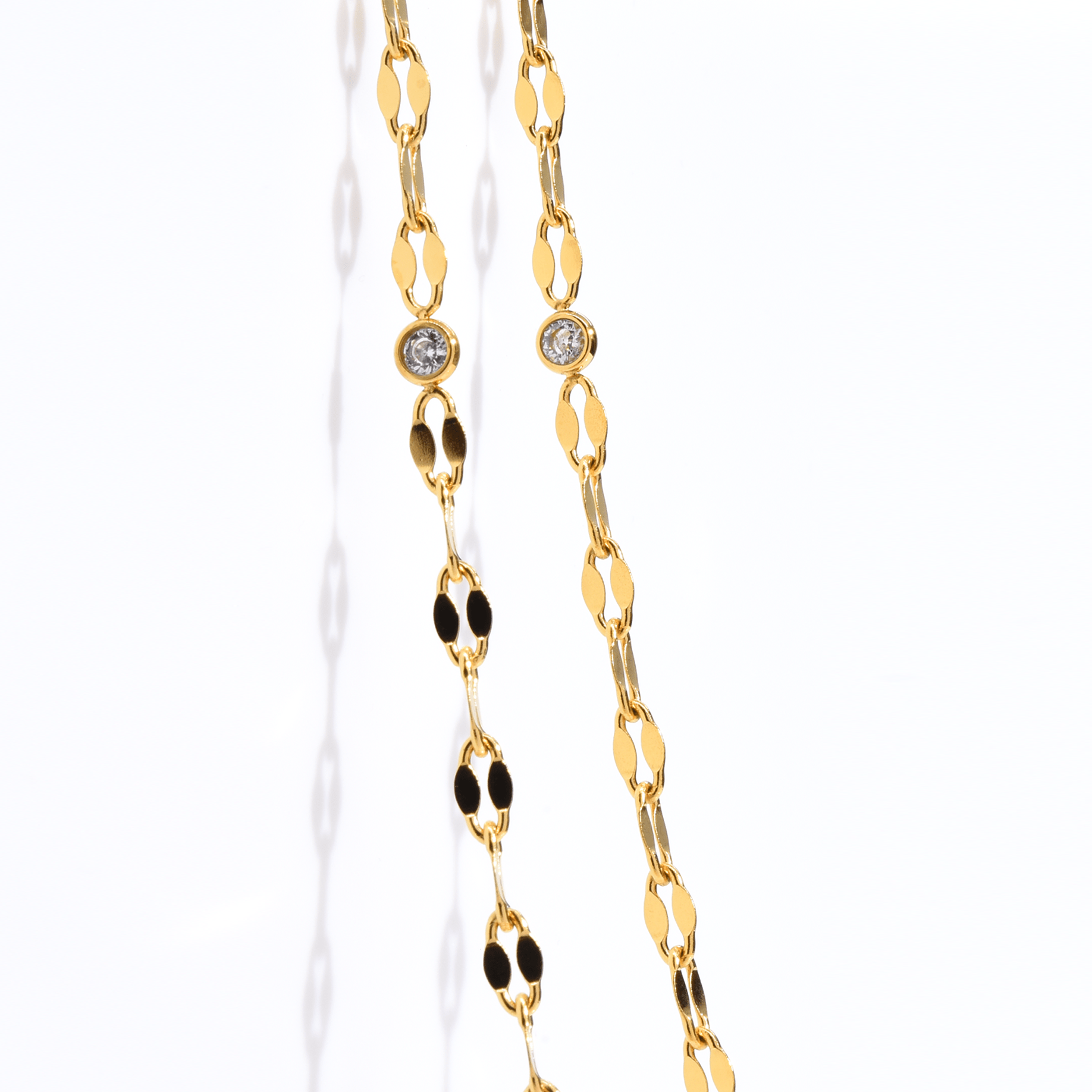 A soft, gold-tone chain with a central CZ stone is shown elegantly resting on skin, styled as both anklet and bracelet. It shimmers as the model moves gently, highlighting the chain’s flexibility and detail.