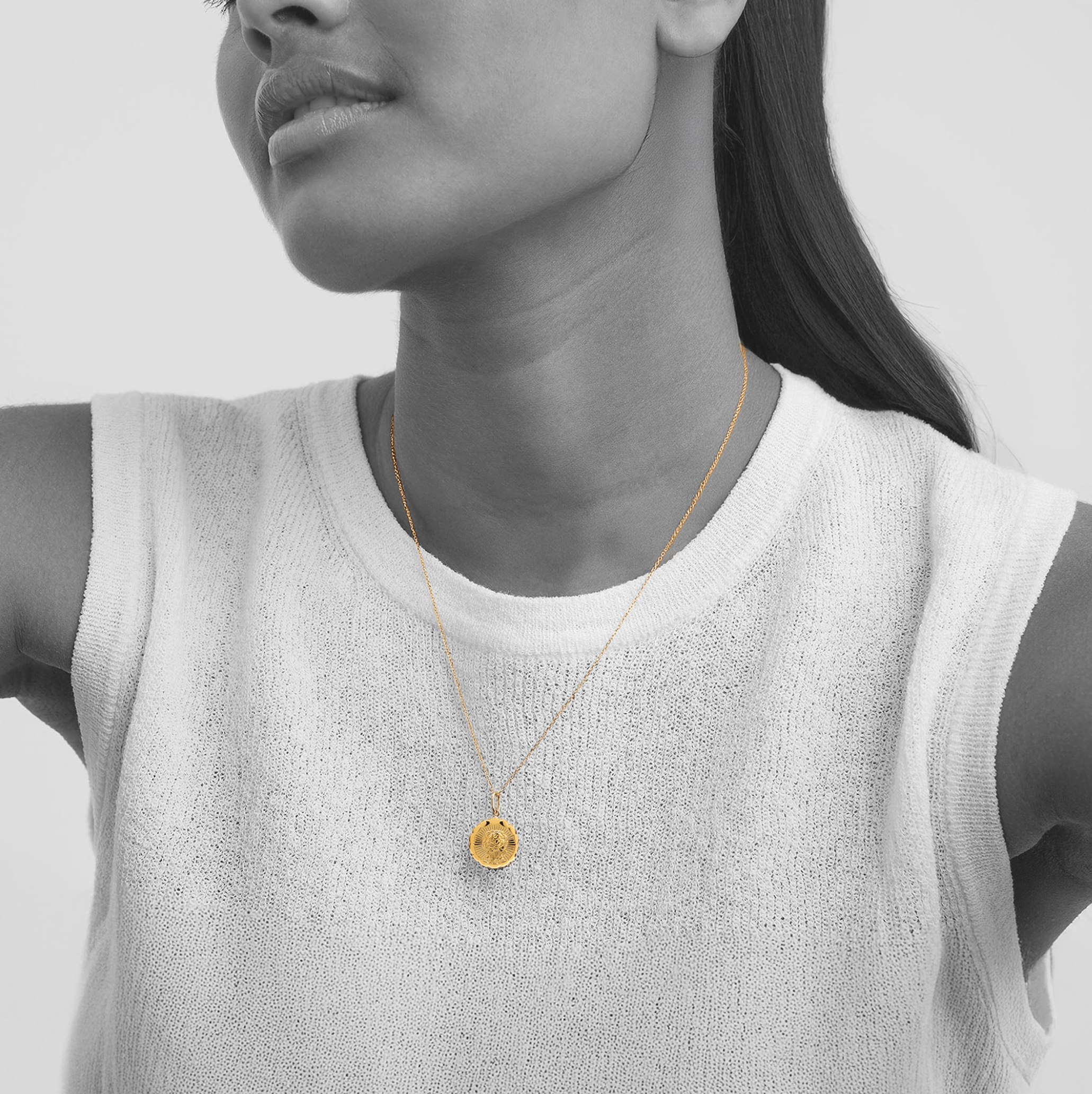 Woman wearing a gold necklace with a pendant against a neutral background