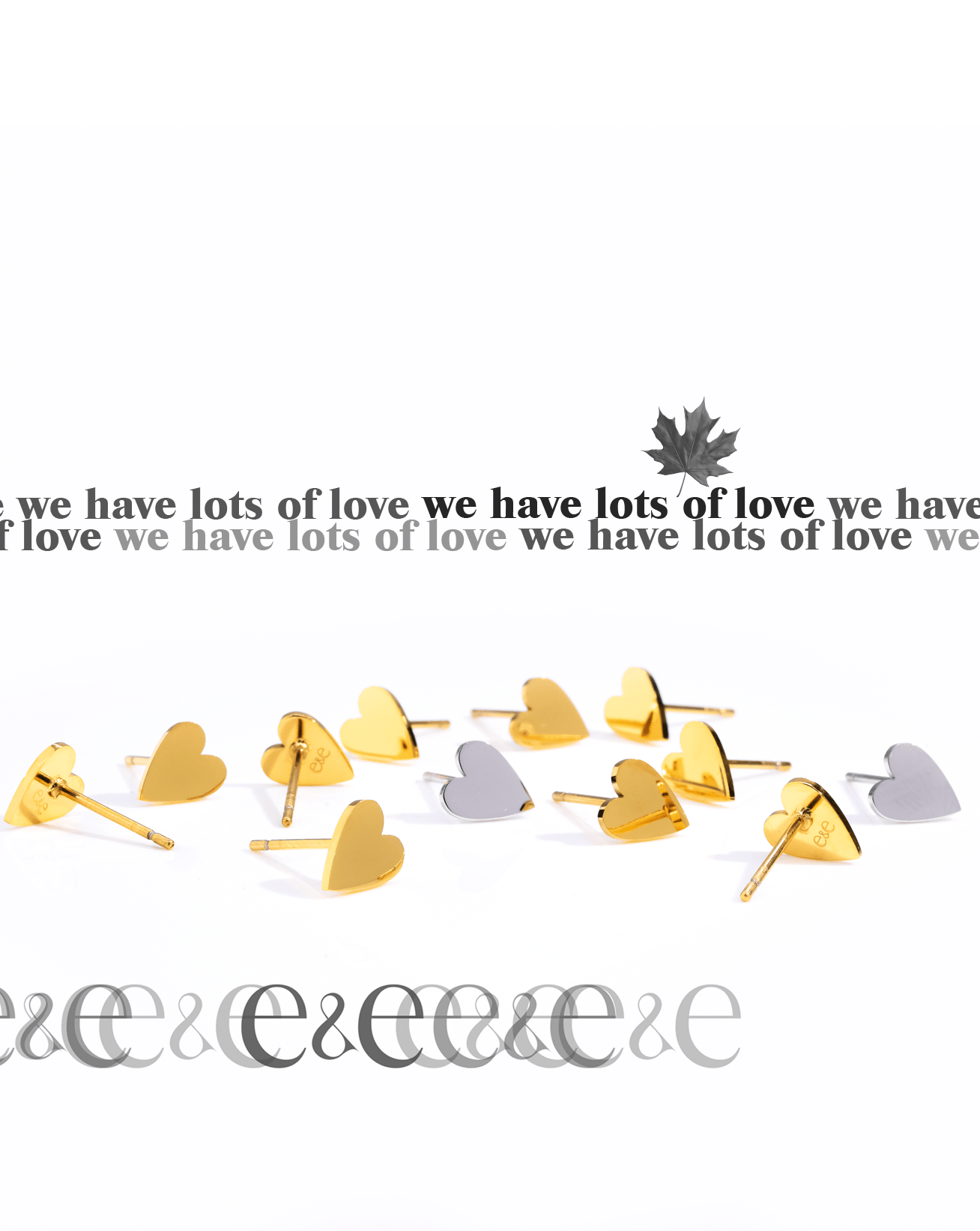 Minimalist photo of gold and silver heart-shaped stud earrings arranged in a scattered line across a white surface. A repeating phrase “we have lots of love” is layered above with a small maple leaf motif.